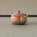 Small reddish shino-glazed lidded pouring vessel (houhin) on a tatami mat.