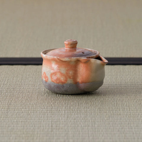 Small reddish shino-glazed lidded pouring vessel (houhin) on a tatami mat.