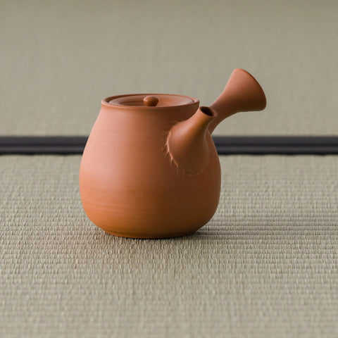 Orange-red kyusu with the side handle angled toward the viewer