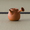 Side view of the smooth orange-red kyusu showing the spout and side handle