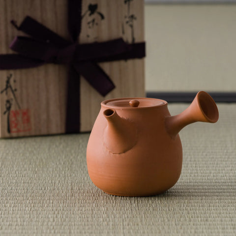 Bright orange-red shudei side-handle kyusu with a smooth polished surface, shown with its wooden box, spout to the right