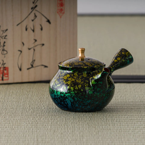 Green-and-gold tokoname side-handle kyusu with dense gold floral pattern, shown with its wooden box, spout to the right