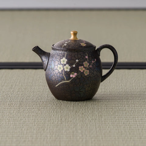 Dark bronze tokoname teapot with a rear loop handle and gold lid knob, spout to the right, floral accents near the base