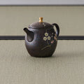 Rear three-quarter view of the bronze teapot showing the upright loop handle