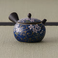 Dark brown side-handle kyusu with blue-and-white cherry-blossom decoration, spout to the left on tatami