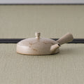 Side view of the low beige kyusu showing its broad flat body and side handle