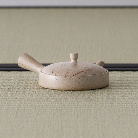 Cream-colored flat kyusu teapot, three-quarter view with the spout to the right