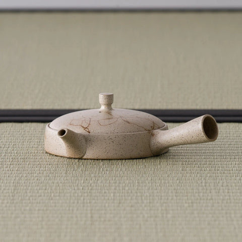 Pale beige low, flat side-handle kyusu with fine brushed-line decoration, spout to the left on tatami