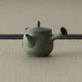 Side view of the sage-green kyusu showing the hollow side handle and engraved motif