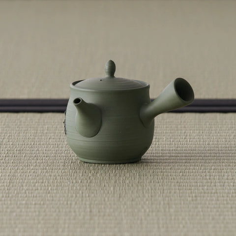 Side view of the sage-green kyusu showing the hollow side handle and engraved motif