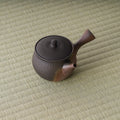 The whole chattered-texture kyusu shown at a distance on tatami, spout to the right