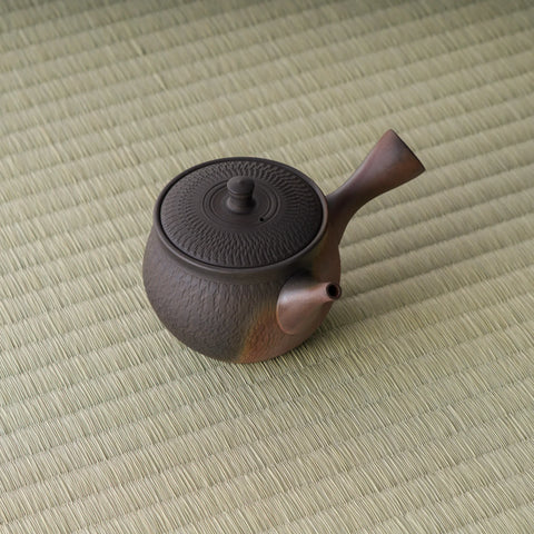 The whole chattered-texture kyusu shown at a distance on tatami, spout to the right
