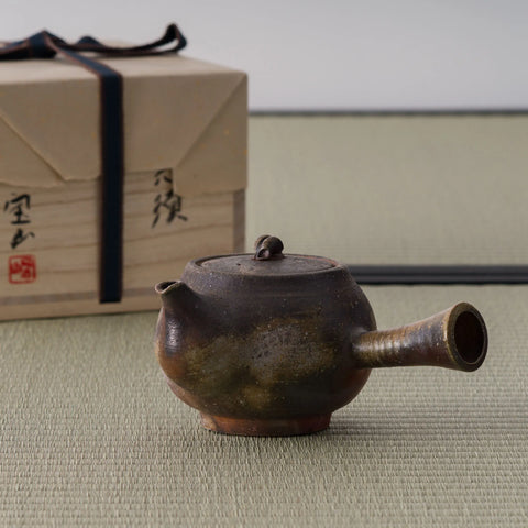 Wood-fired tokoname side-handle kyusu in earthy brown tones shown with its wooden storage box, spout to the right