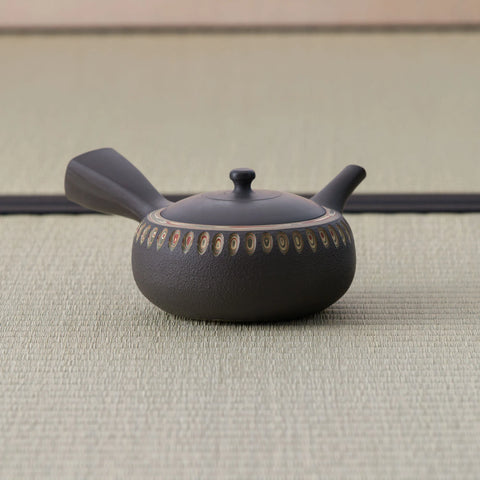 Dark stoneware kyusu teapot with a side handle and a band of carved oval motifs, side view.