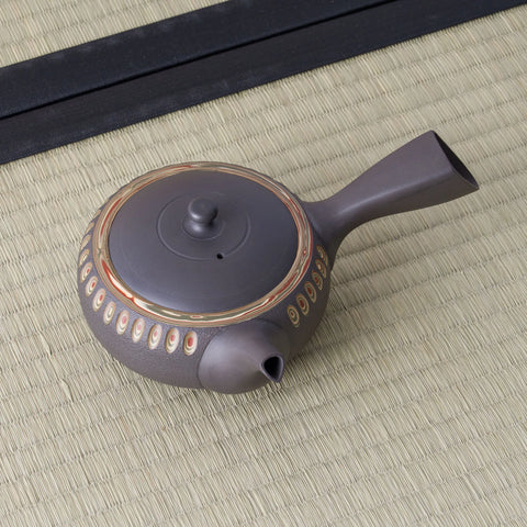 Dark clay kyusu teapot with a side handle and carved oval band, viewed from above, on a tatami mat.