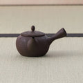 Dark brown kyusu teapot with a side handle, basket-weave carved body and lid, side view on a tatami mat.