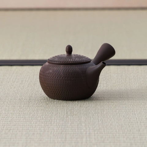 Dark brown kyusu teapot with a side handle, combed body and lid, side view on a tatami mat.