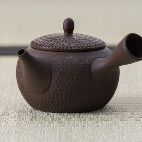 Dark purple-brown clay kyusu with a carved basket-weave texture and lid, side view.