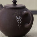 Dark purple-brown teapot with a loop handle and white wisteria inlay, close side view.
