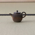 Brown wood-fired kyusu with a loop handle and lid, side view on a tatami mat.