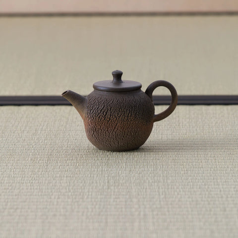 Brown wood-fired kyusu with a loop handle and lid, side view on a tatami mat.