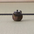 Brown wood-fired kyusu with a loop handle and textured body, side view on a tatami mat.
