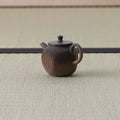 Brown wood-fired kyusu with a loop handle, textured body and lid, side view on a tatami mat.