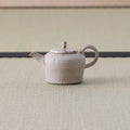 Speckled beige kyusu teapot with a loop handle, side view on a tatami mat.
