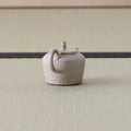 Speckled stoneware kyusu teapot with a loop handle, side view on a tatami mat.
