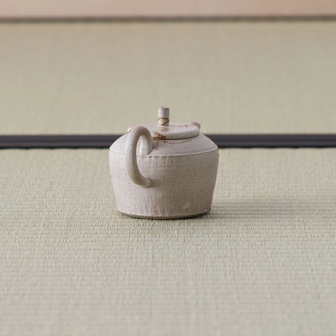 Speckled stoneware kyusu teapot with a loop handle, side view on a tatami mat.