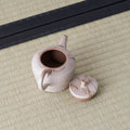 Speckled stoneware kyusu with its lid removed, revealing the mesh strainer inside, on a tatami mat.