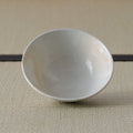 Cream-white glazed shallow bowl viewed from above with subtle orange markings, on a tatami mat.