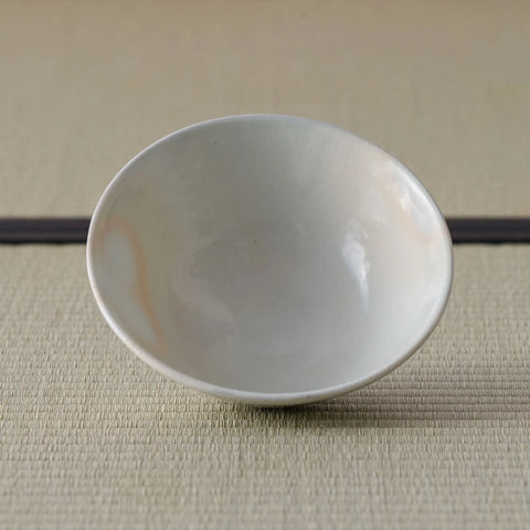 Cream-white glazed shallow bowl viewed from above with subtle orange markings, on a tatami mat.