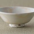 Cream-white glazed rice bowl with a faint pink blush, side view on a tatami mat.