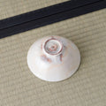 Cream-white glazed bowl inverted to show its spiral-carved foot, on a tatami mat.