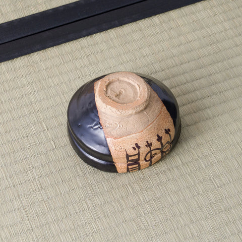 Underside of a black Kuro-Oribe chawan showing its unglazed foot and painted clay panel wrapping the side.