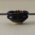 Back view of a black kutsu-gata chawan with gently squared rim, raised on a light clay foot.
