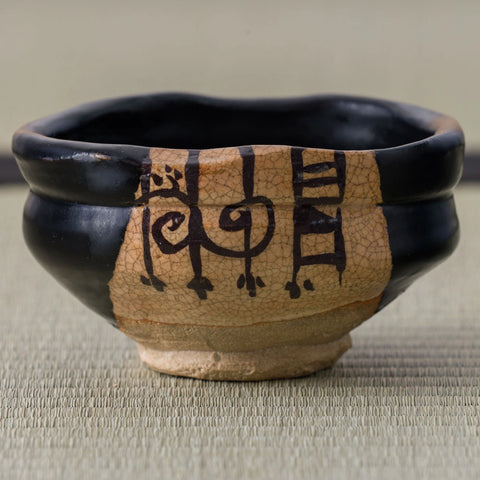 Close-up of the crackled clay window and bold dark brushwork on a black Oribe-glazed chawan.