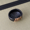 Overhead view of a black chawan showing spiral throwing marks inside and the painted panel at its rim.
