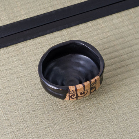 Overhead view of a black chawan showing spiral throwing marks inside and the painted panel at its rim.