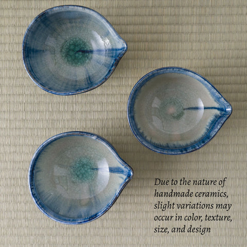 Three handmade ceramic tea bowls with blue and green glaze variations, arranged on a beige tatami mat background with a text overlay explaining variations in handmade ceramics.