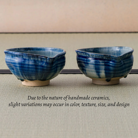 Two handmade blue glazed ceramic bowls with a textured, hand-painted finish and small footed bases, displayed on a textured tatami surface with a text overlay explaining variations in handmade ceramics.