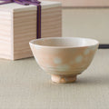 Pale peach chawan with soft white spotted kase-style glaze, set in front of its ribbon-tied wooden storage box.