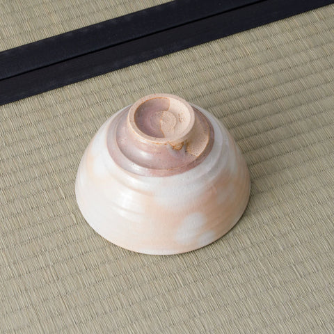 Spotted peach-glazed chawan resting on its side, showing the unglazed foot and swirled base.