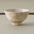 Front view of a kase-spotted chawan with pale orange glaze and a short bare clay foot on tatami.
