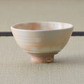 Side view of a peach-toned chawan with white spotted glaze, subtle throwing rings, and unglazed foot.
