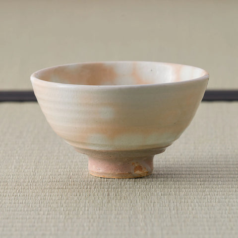 Side view of a peach-toned chawan with white spotted glaze, subtle throwing rings, and unglazed foot.