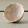Tilted chawan revealing a glossy pale interior and soft white spots over peach glaze.