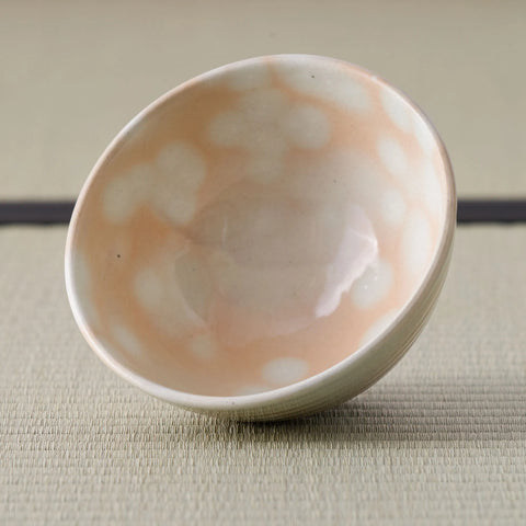 Tilted chawan revealing a glossy pale interior and soft white spots over peach glaze.