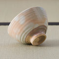 Chawan tipped on its side to show the carved foot ring and layered bands of peach and cream glaze.